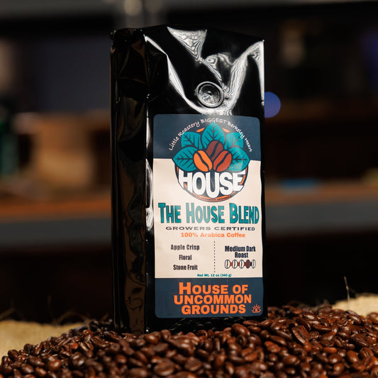 Bag of The House Blend coffee from House of Uncommon Grounds on a bed of roasted beans