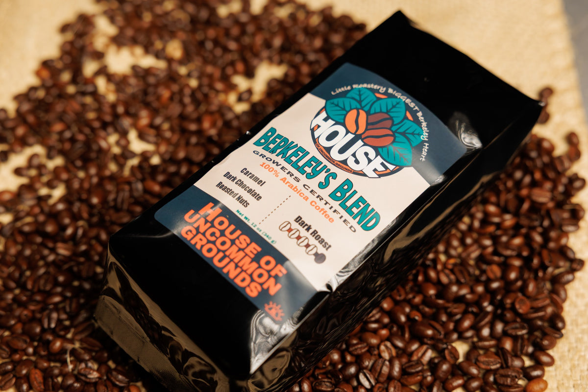 A black bag of Berkeley’s Blend lying on roasted coffee beans