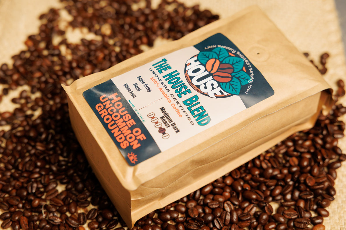 A kraft bag of The House Blend lying on roasted coffee beans
