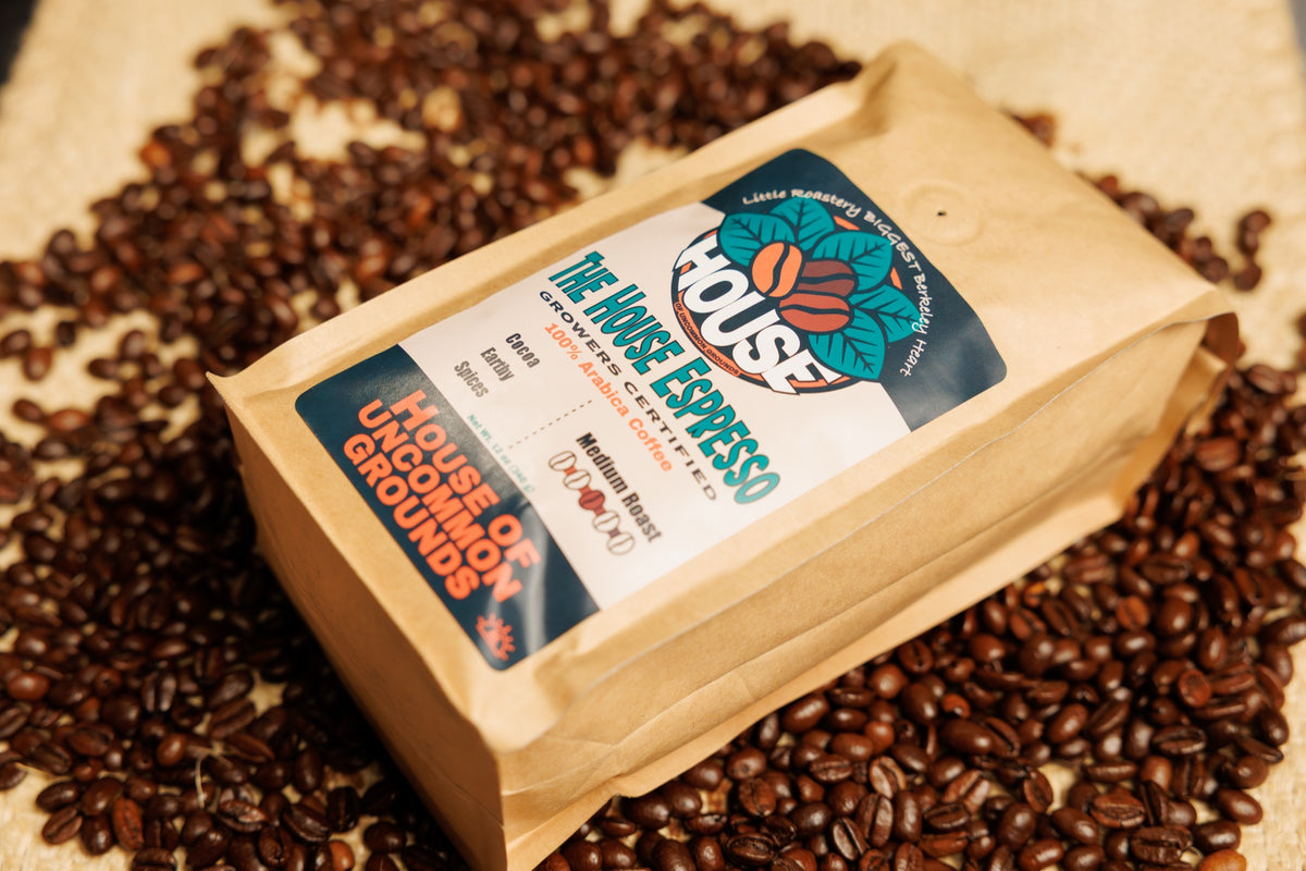 A kraft bag of The House Espresso lying on roasted coffee beans