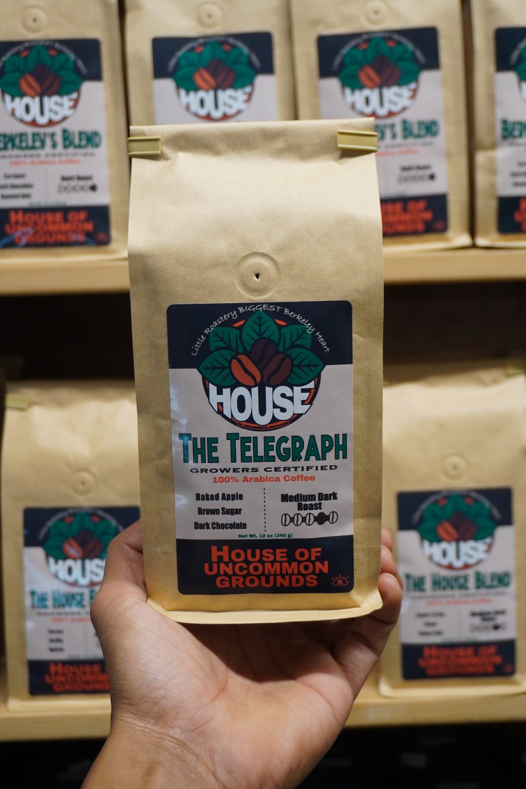 A bag of The Telegraph with its kosher mark, held up in front of the House coffee shelves